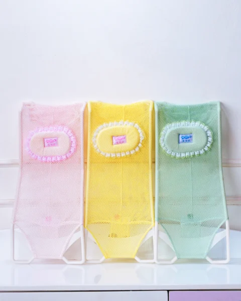 Group shot of three colorful baby bath support net slings (pink, yellow, green) side-by-side.