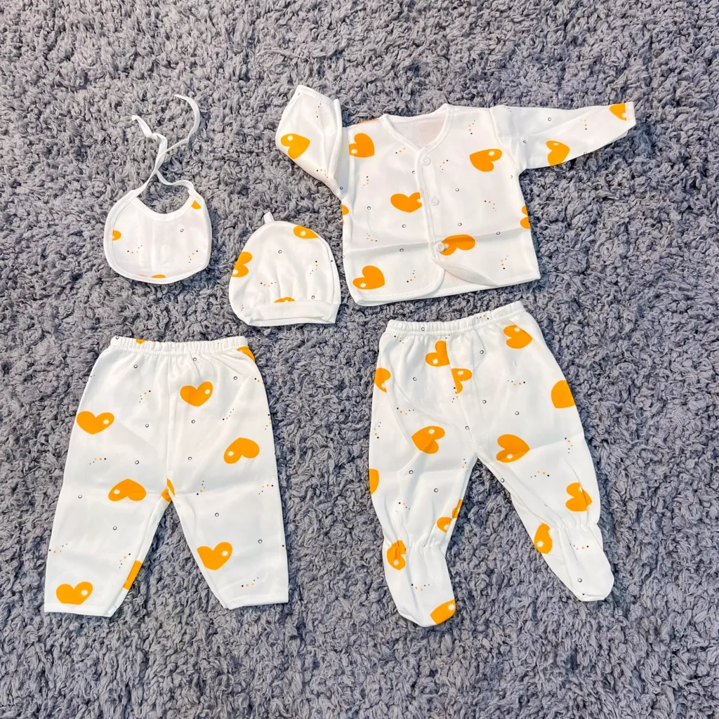 5-piece newborn baby receiving set with a yellow heart print, including a long-sleeve top, two pairs of pants, a cap, and a bib, displayed on a soft grey background.