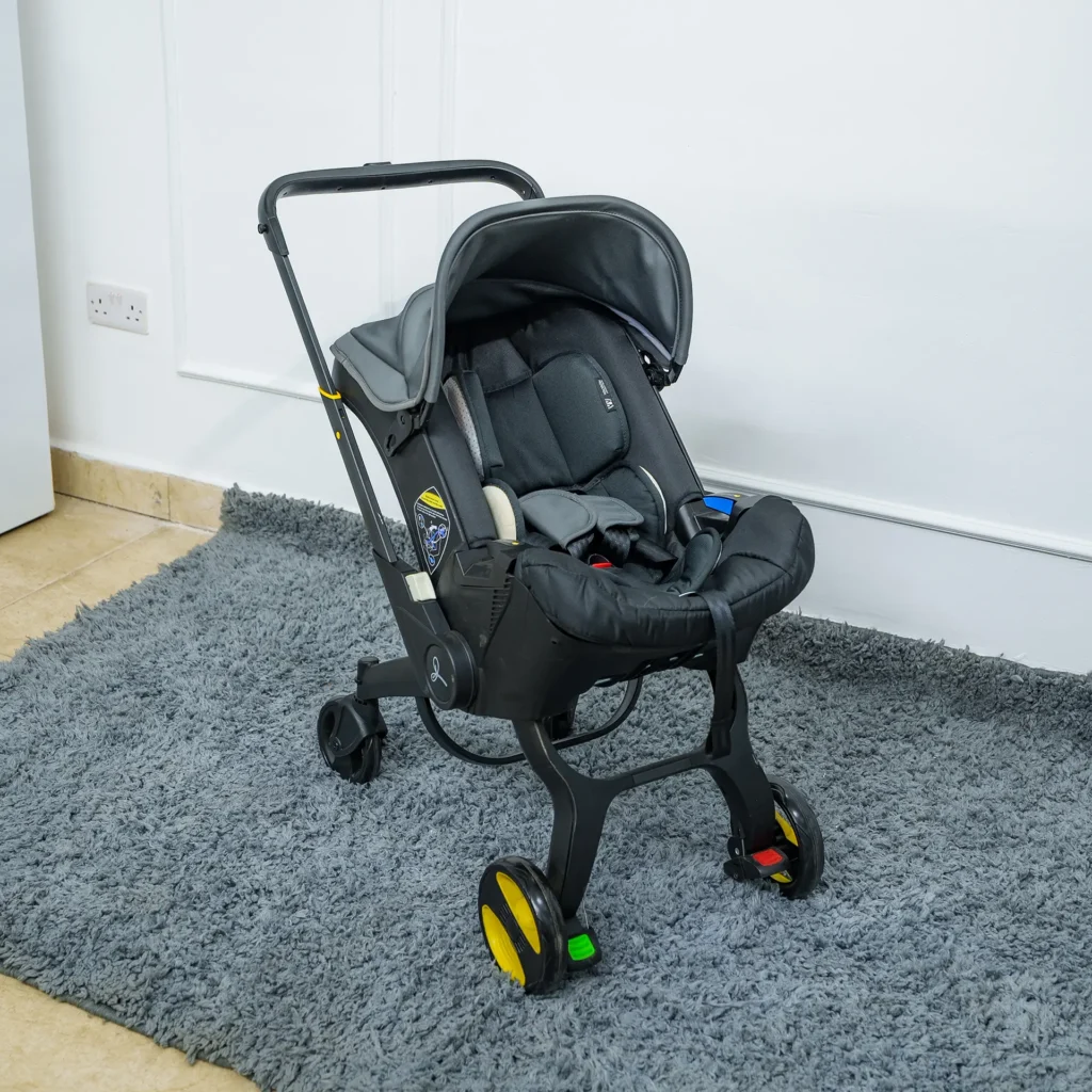 Side view of the 4-in-1 car seat stroller in stroller mode with the handle extended, wheels deployed, and canopy partially raised, displayed on a grey rug.