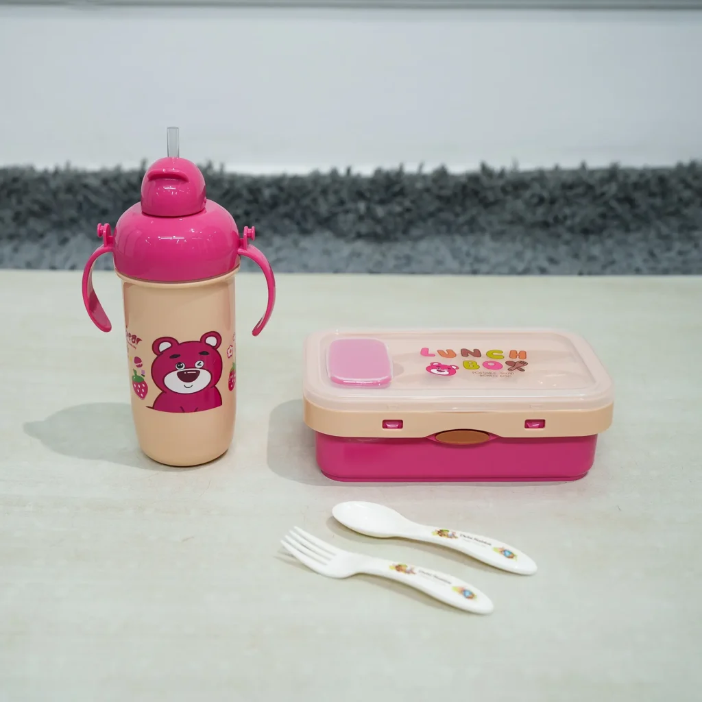 Pink and beige kids lunch set featuring a rectangular lunch box, a handled sippy cup-style water bottle with a pink bear design (resembling Lotso from Toy Story) and pop-up straw, and a white plastic fork and spoon with pattern, displayed on a light surface.