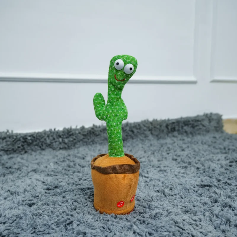 Green plush dancing cactus toy with large eyes and a smile, standing in a brown pot on a grey rug.