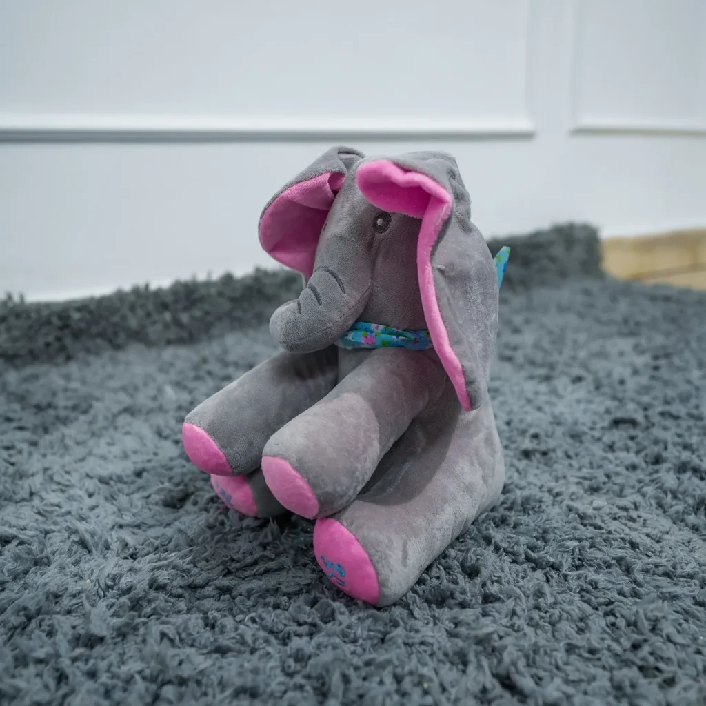 Plush gray elephant soft toy with pink ears and feet, sitting on a soft gray rug—ideal for babies and toddlers, available at Zawadi Baby Shop.