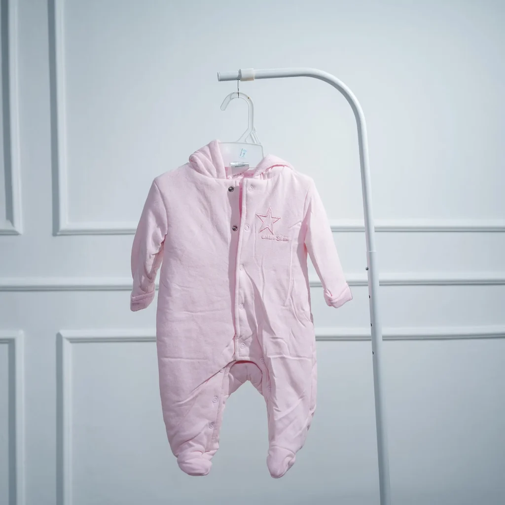 Light pink baby romper with hood and footies, crafted from soft heavy cotton, hanging on a white plastic hanger against a paneled white wall.