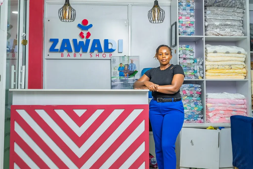 Founder of Zawadi Baby Shop in Nairobi standing at the reception desk with the company logo and stocked baby blankets in the background.