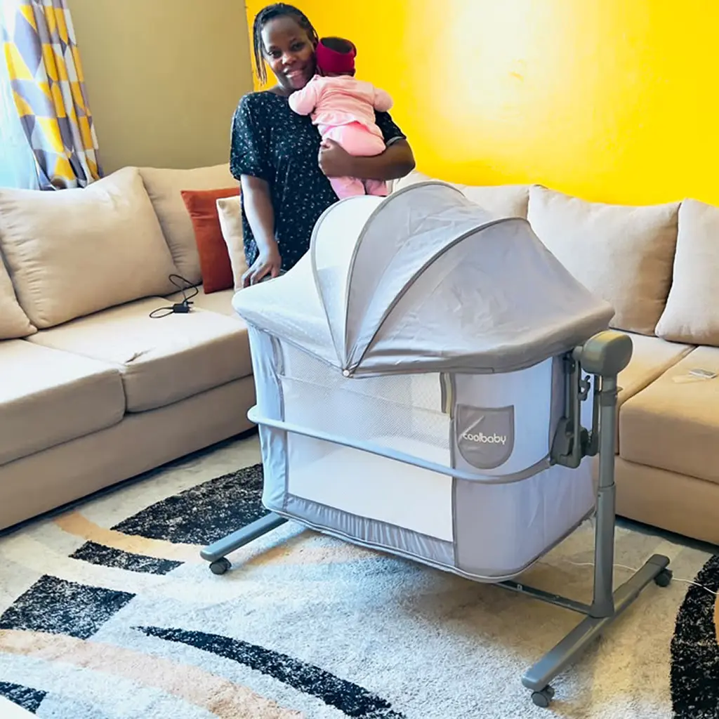 Coolbaby 2 In 1 Electric Bassinet 2 Mum Holding Her Baby Beside The 2 In 1 Electric Bassinet With Its Canopy, At Zawadi Baby Shop Nairobi.